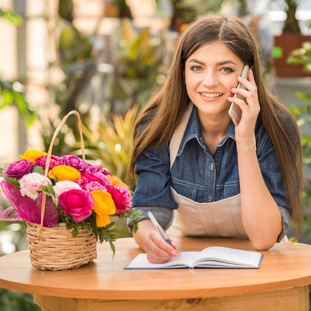 young female florist talking on the phone while taking notes at a flower shop