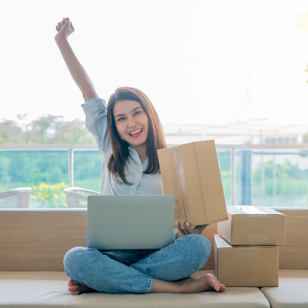 happy young woman with shopping boxes next to her and a laptop on her lap