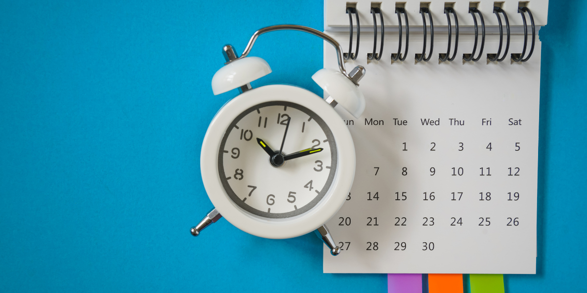 a tabletop calendar, alarm clock, and colorful post its against a blue background