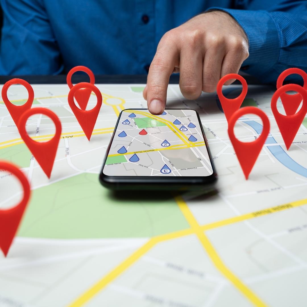 Close-up of a person navigating a city map on a phone, with 3D red map markers placed around the paper map.